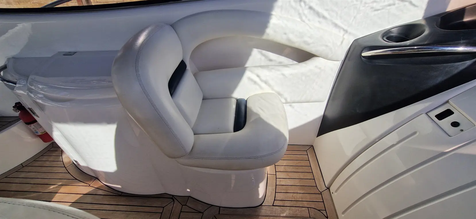 One ergonomic white boat seat positioned beside a sleek black panel, with wooden flooring and sunlight casting shadows.